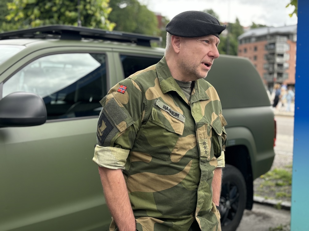 militær person, med beret på hode og kamuflasje uniform, ved siden av grønt militært kjøretøy.