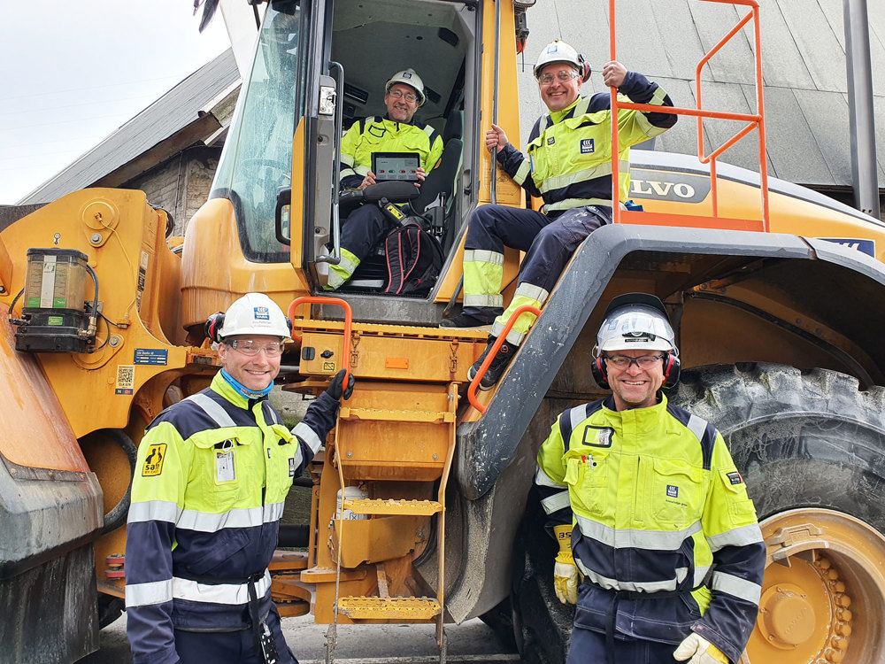 four persons standing next to or sitting on a payloader
