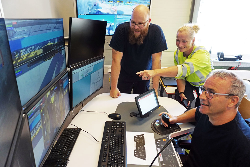 tre personer på kontor peker på monitorer som overvåker lasteoperasjoner