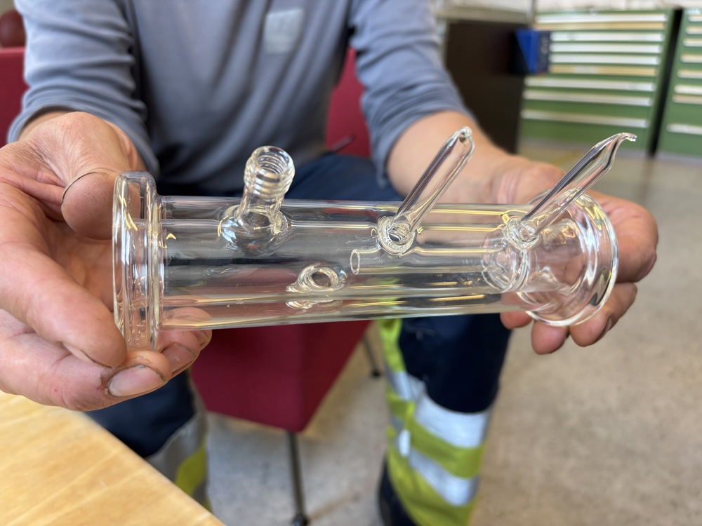 two hands holding small tubular glass structure with small pipes
