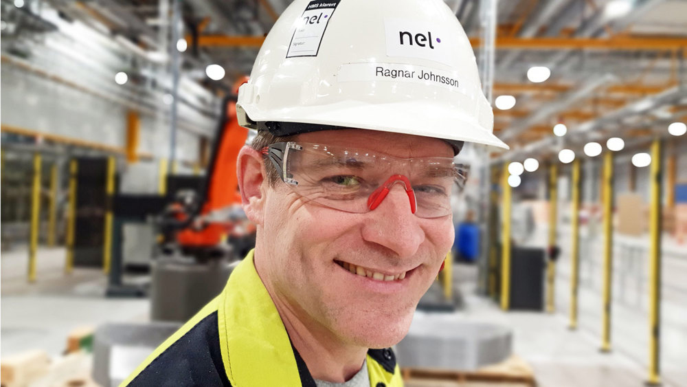 portrait of man, smiling, posing,  wearing white helmet and goggles, standing in a procuction hall.