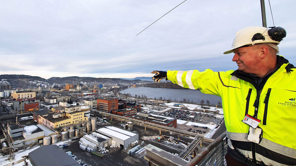 man standing on top of tower, pointing out over the industrial park