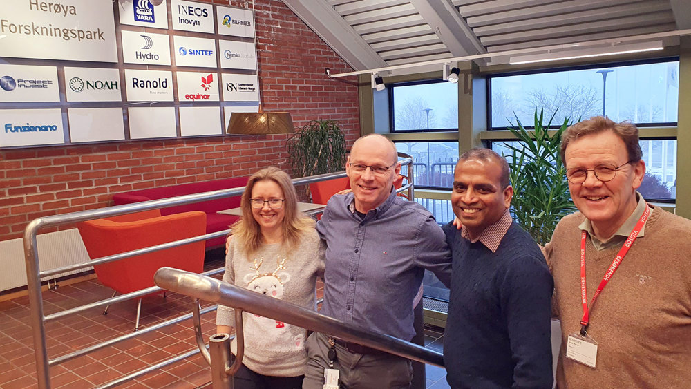 four people standing in the stairs, a reception area, company logoes on the red brick wall, big windows