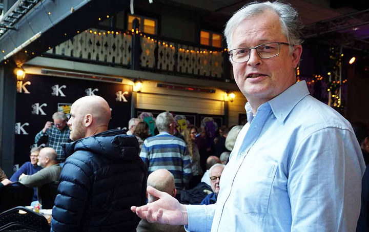 portrait of man, standing in a big room, with a lot of other people