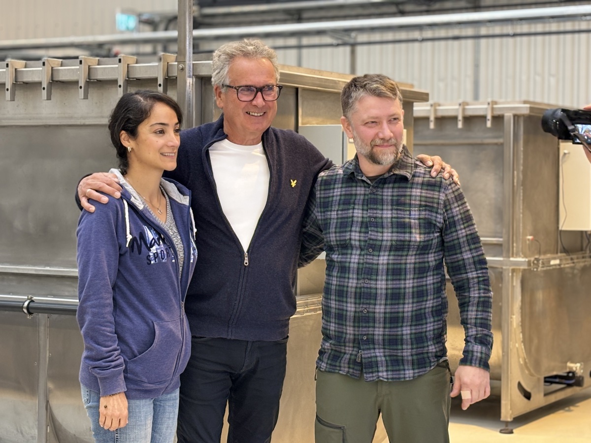 three persons standing together, arms around each others sholders, production equipment, production hall