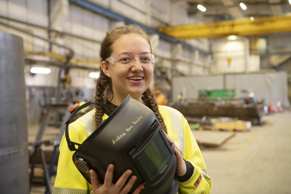 young female apprentice holding a welders facemask in her hands