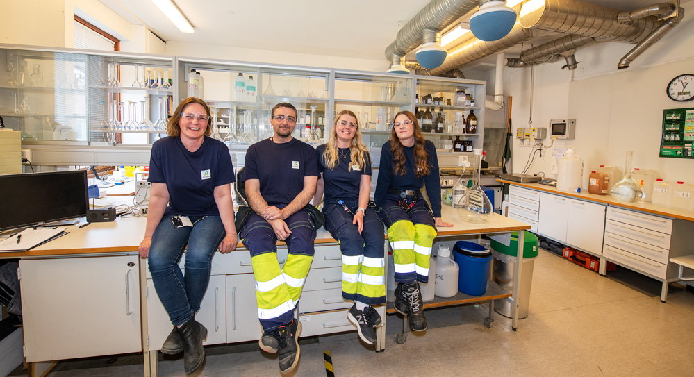 arbeidslag på fire sitter på et bord i et laboratorium med glasskap i bakgrunnnen