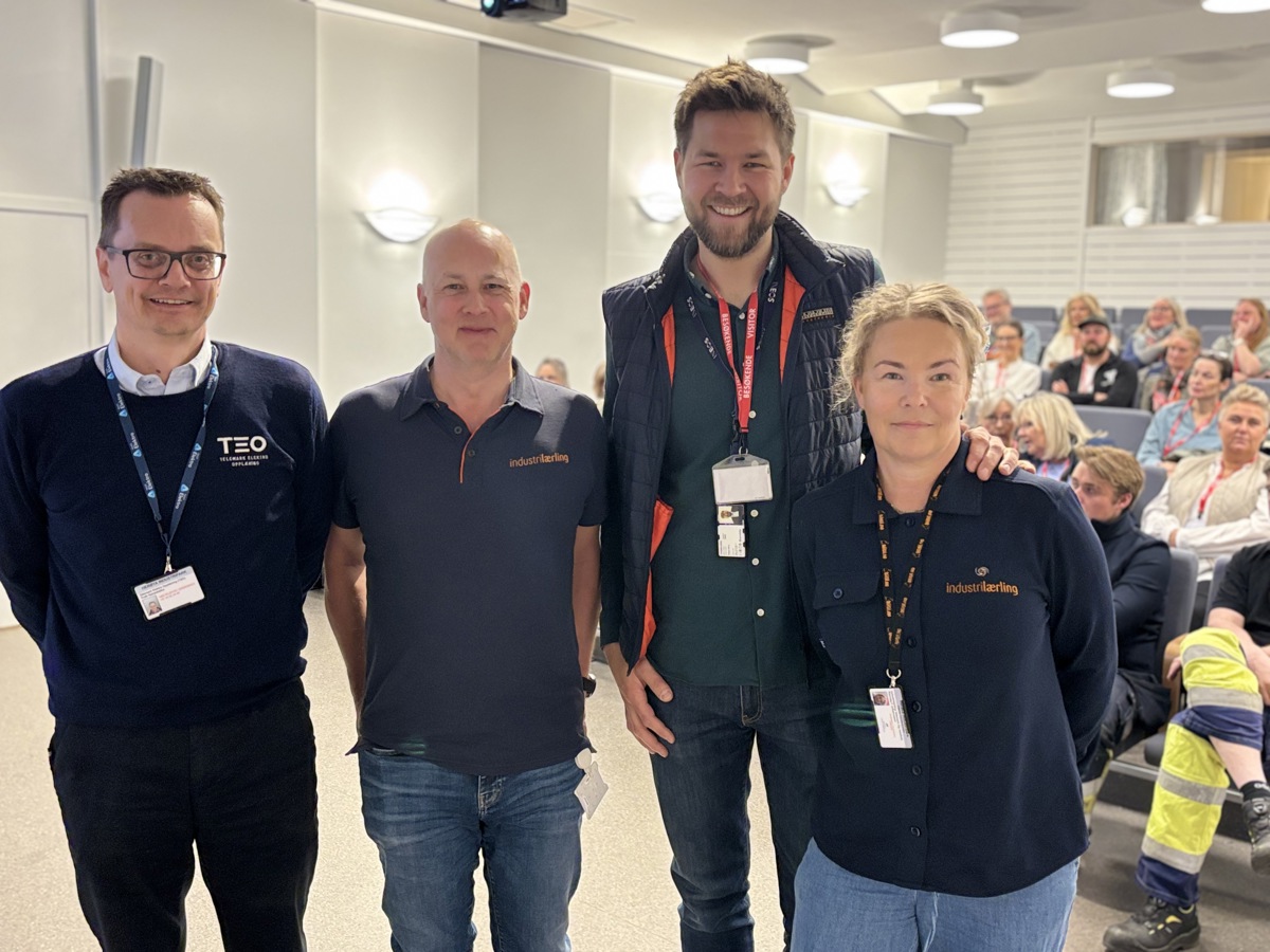 four persons standing in front of a auditorium with a lot of people