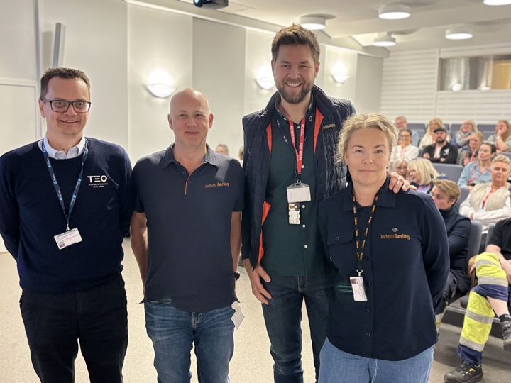 four persons standing in front of a auditorium with a lot of people