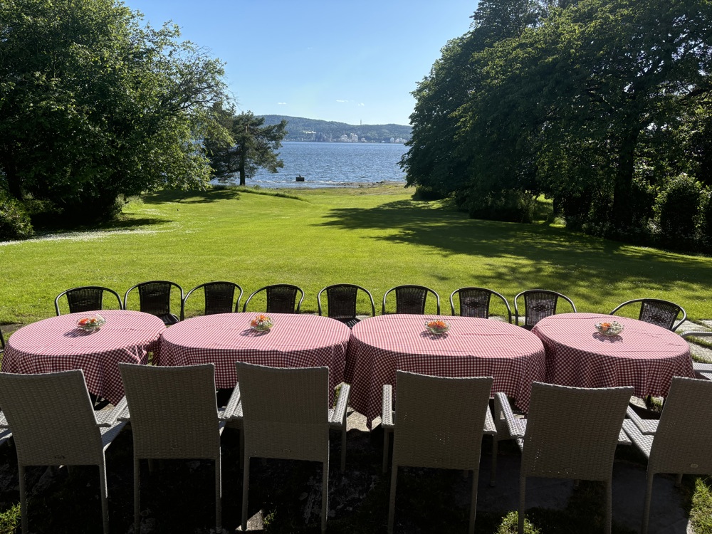 hage med utsikt mot fjorden, runde bord i forkant med rutete duker.