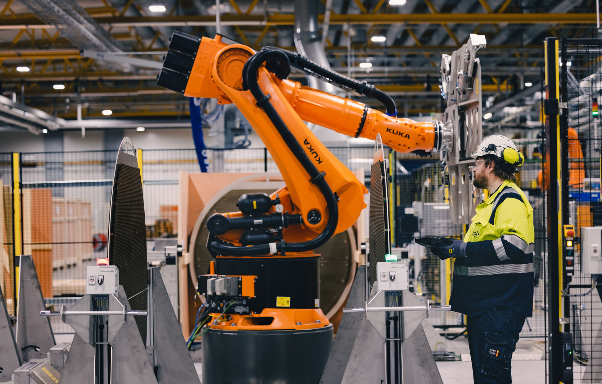 man, beard, white helmet, steering orange robot in production facility