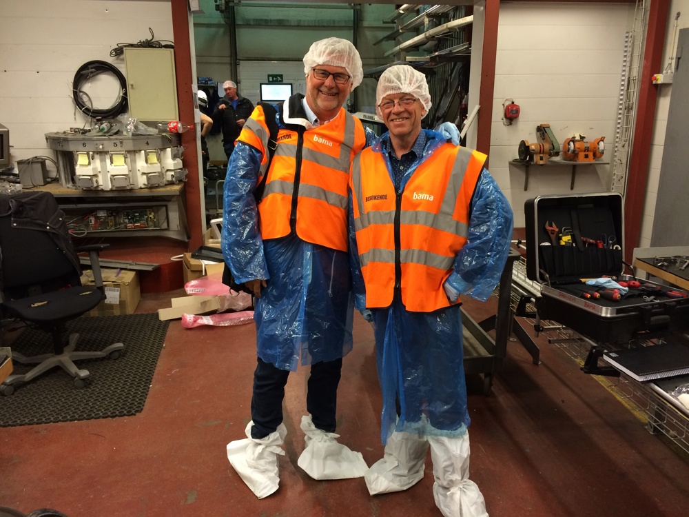 to menn poserer i blå plastikkfrakker, gule vester, plasthetter på hodet og plastposer på skoene.