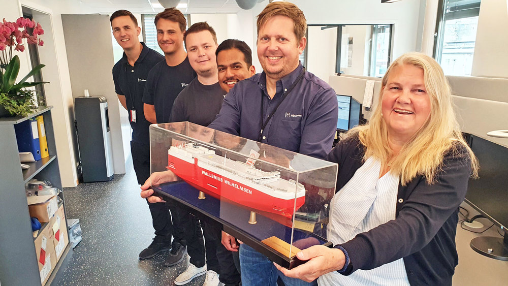 six employees standing in a line holding a ships model in front