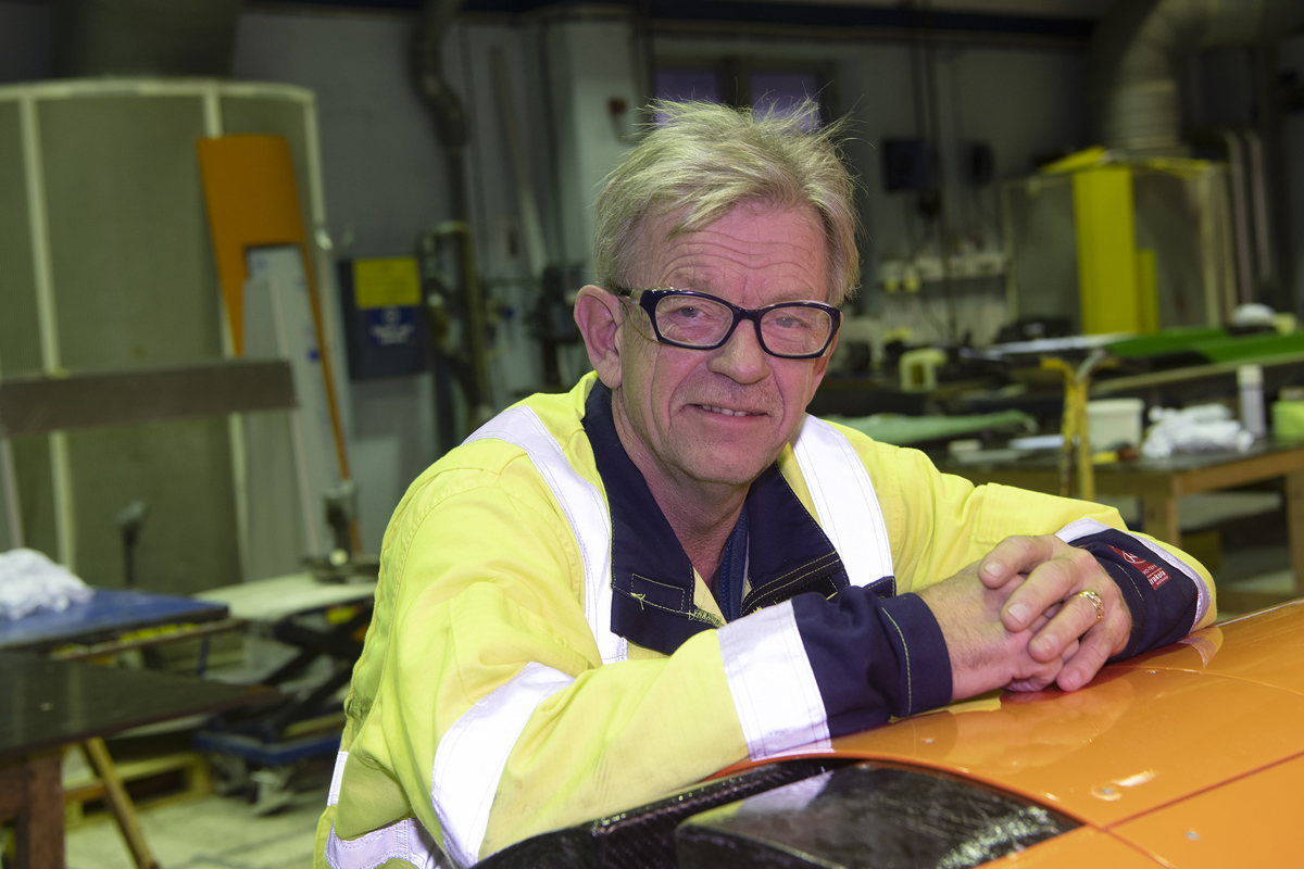 portrett av mann i gul jakke, begge armene ligger på et oransje skrog