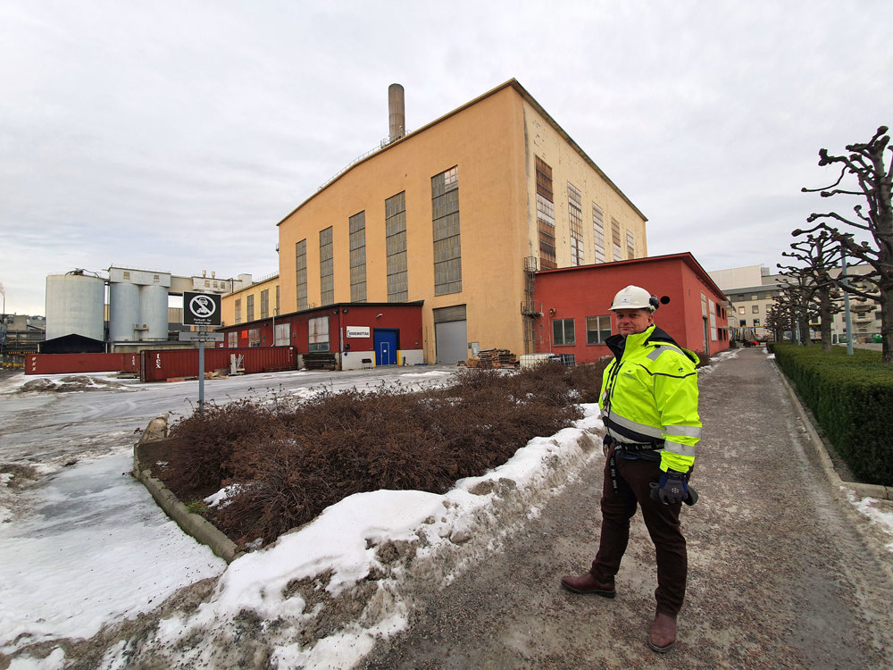 man standing on pavement in industrial park, yellow building in background