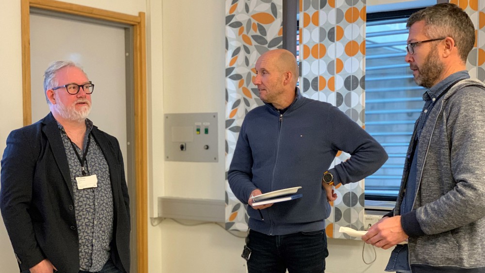 three men standing talking in a meeting room