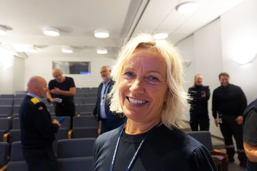 portrett kvinne, smiler, poserer, møtedeltakere i bakgrunnen, auditorium