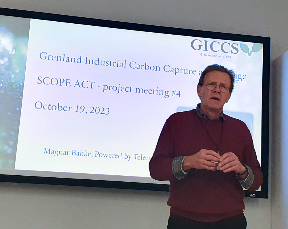 man stands in front of a large screen presenting GICCS on a slide