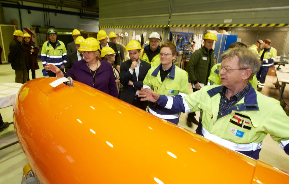 gjester med gule hjelmer besøker verksted og får se skrog undervannsfarkost