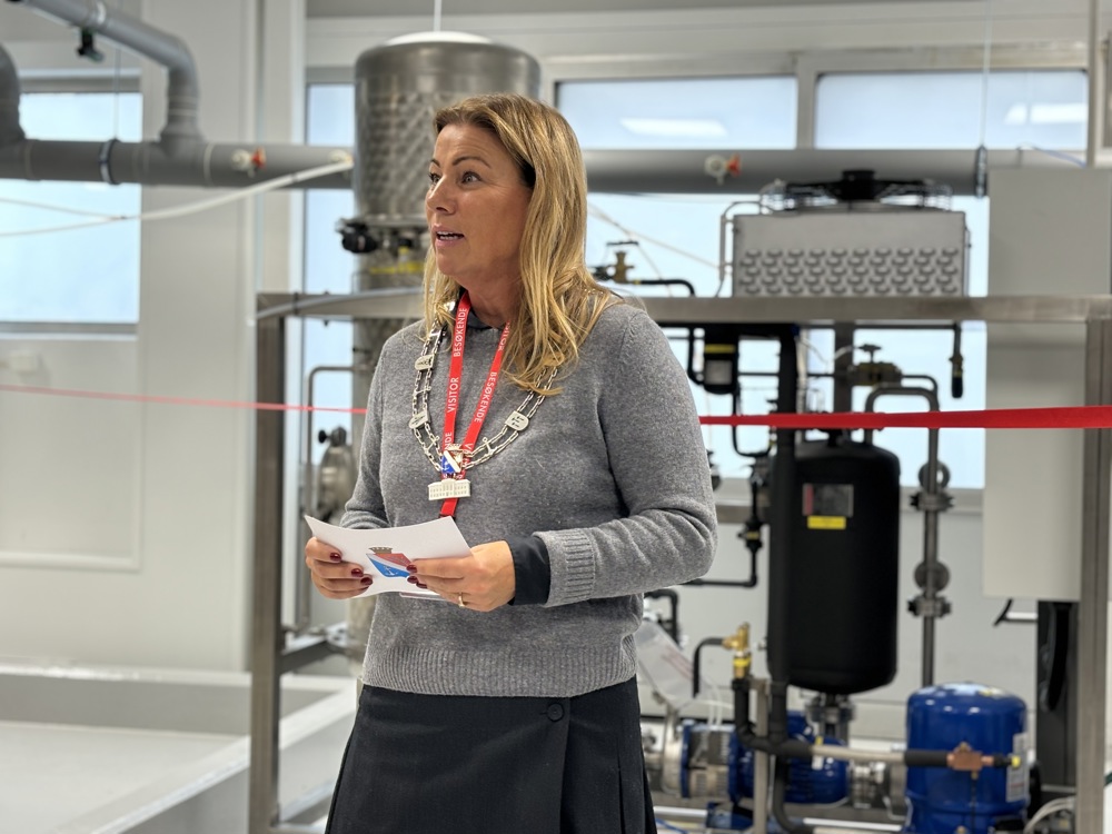 woman in grey jumper, speach, pilot facility in background.