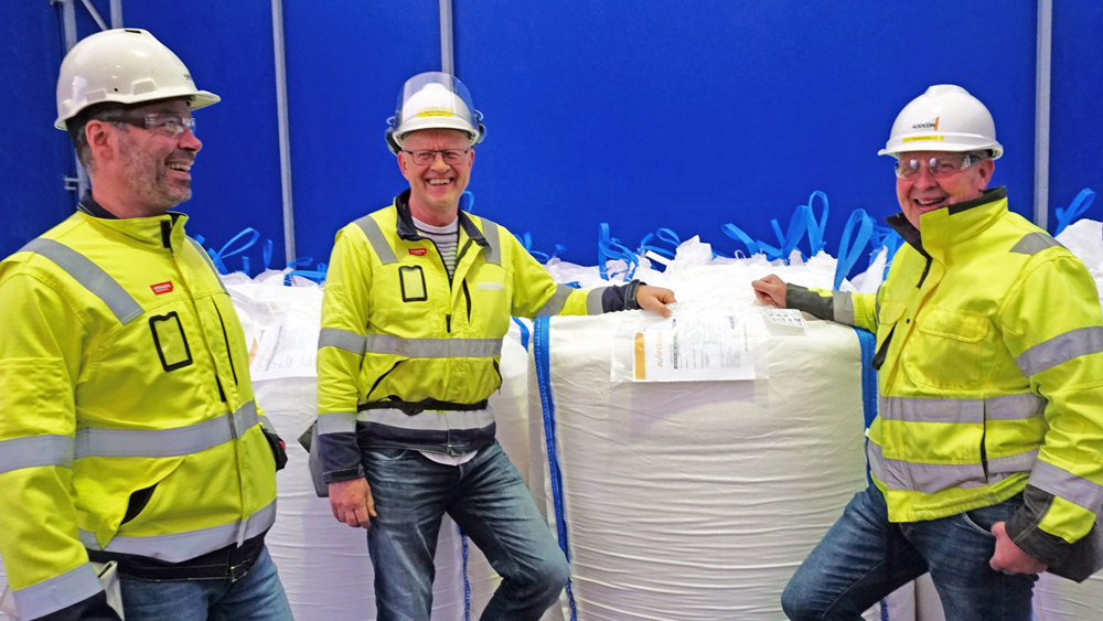 three men in warehouse. Big bag, products