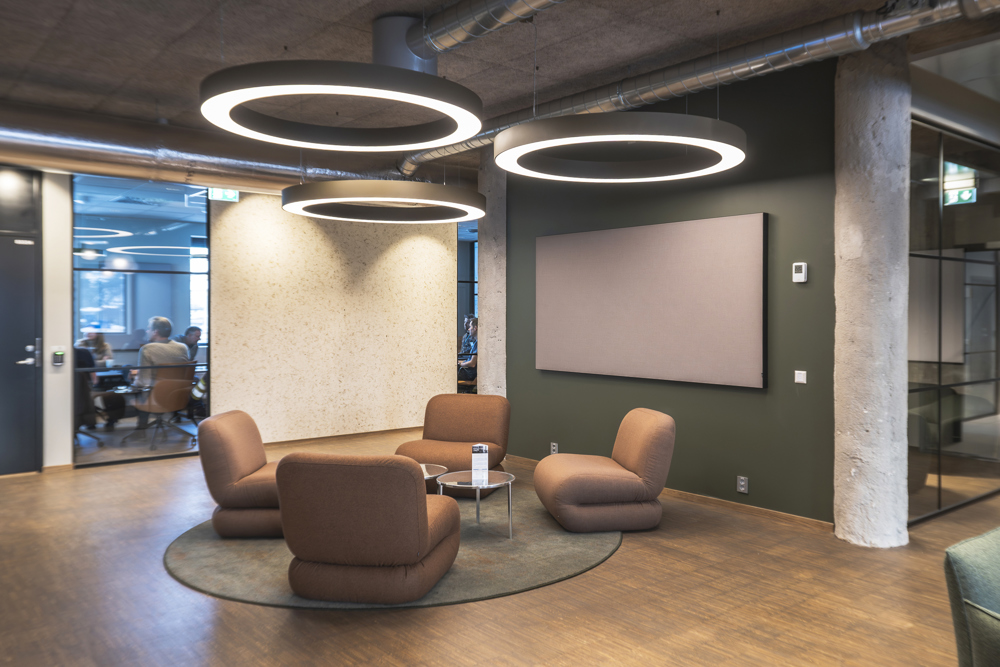 sosial sone utenfor møterom, fire stoler, store ringer med lys i over møblene, betong og trematerialer.