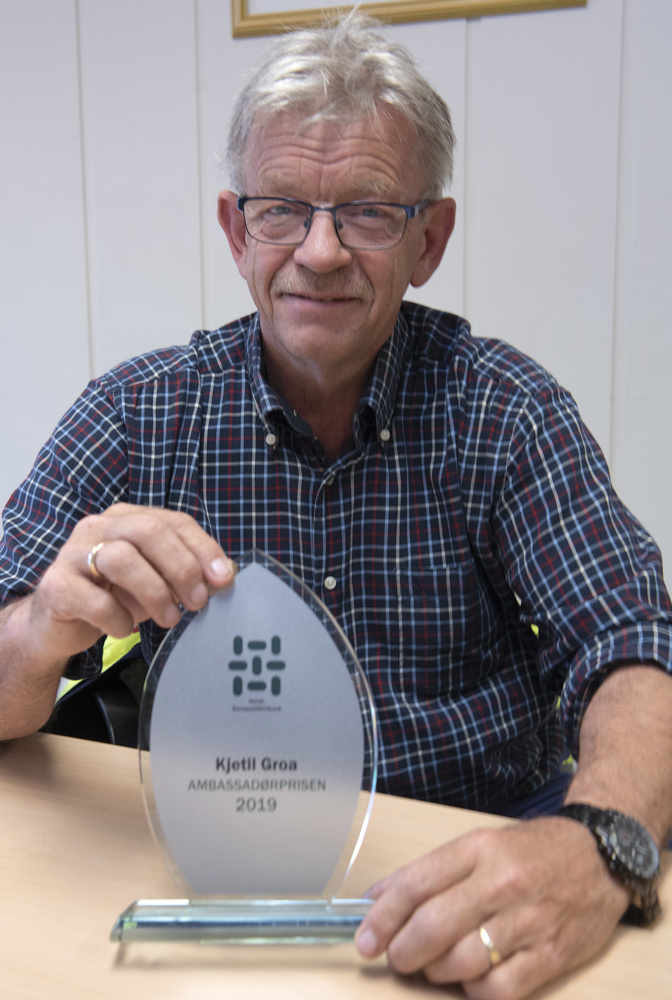 portrett av mann, sitter ved bord, holder i en glassplakett, en pris