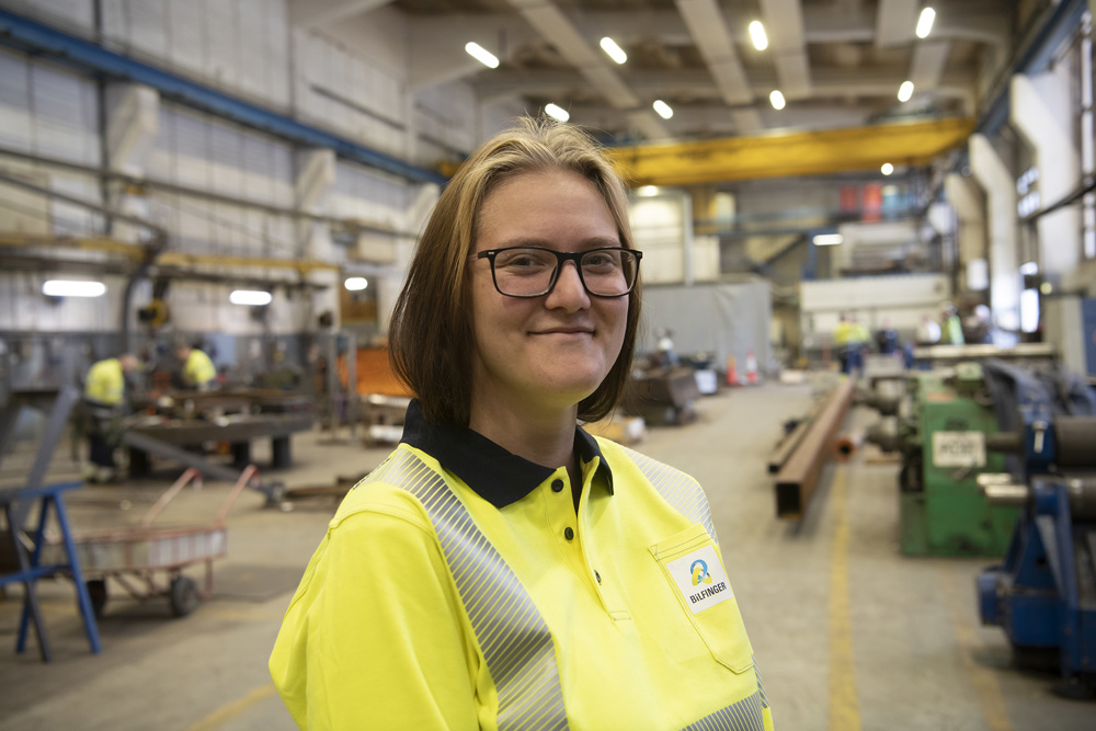 young female apprentice with glasses standing in workshop hall