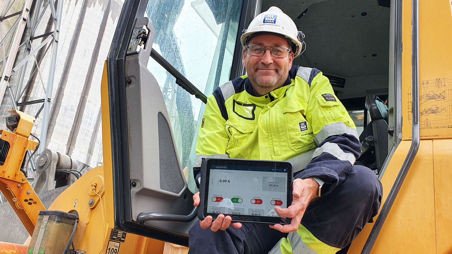 man sitting in the doorframe of a payloader holding an ipad, posing
