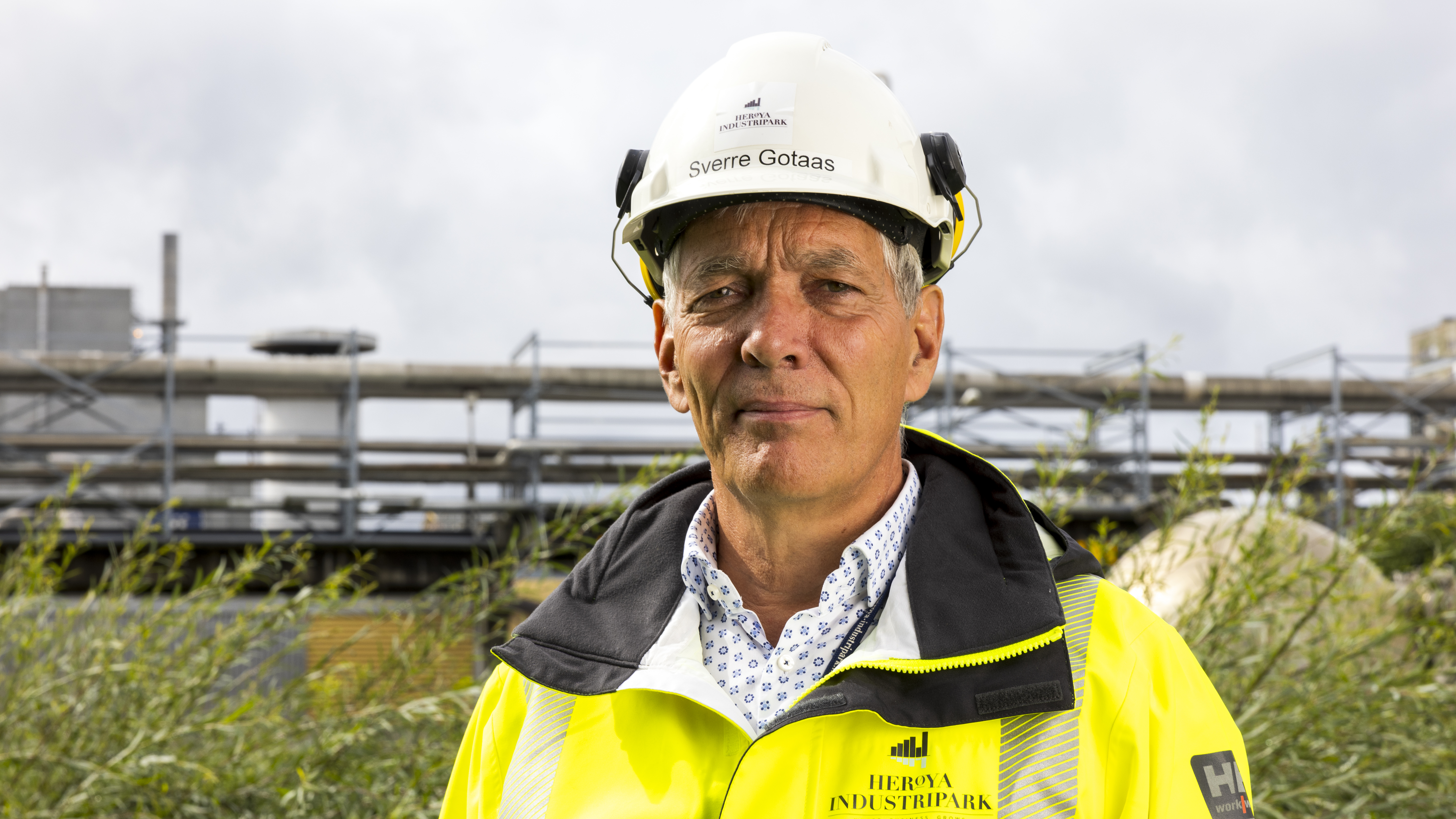 portrait of man, white helmet, yellow jacket, process plant in background