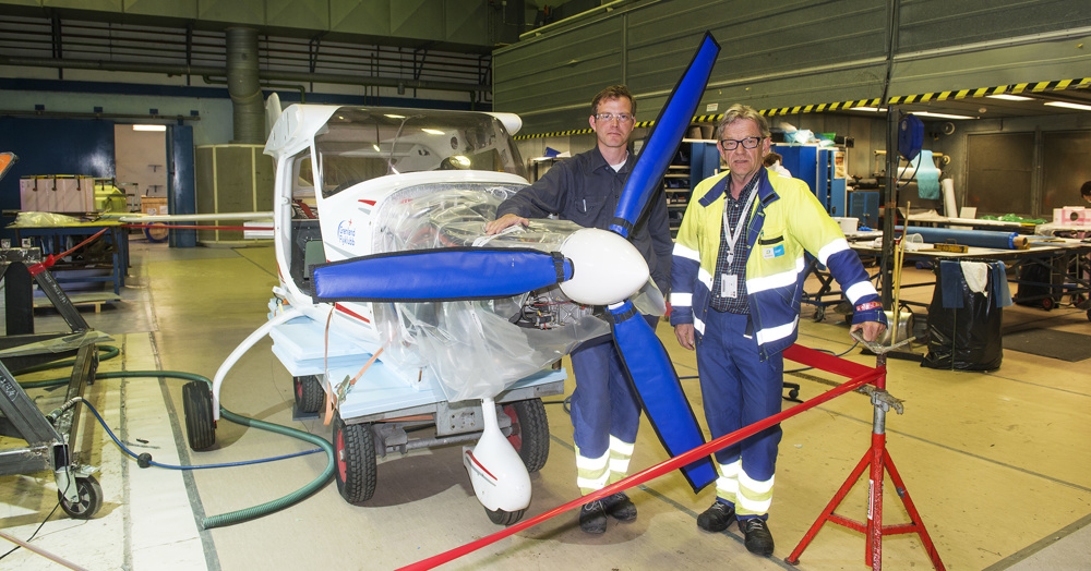 to personer står ved propell på minifly inne i et verksted