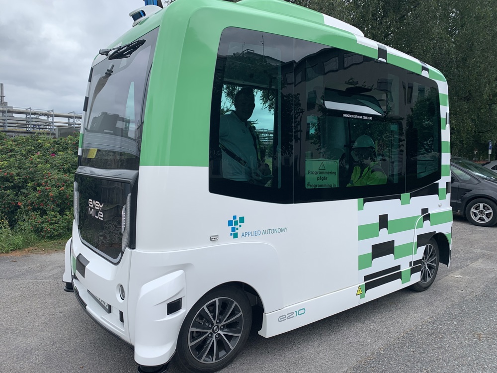 small mini bus, autonomous, self-driving, white and green, parked along a road in the industrial park